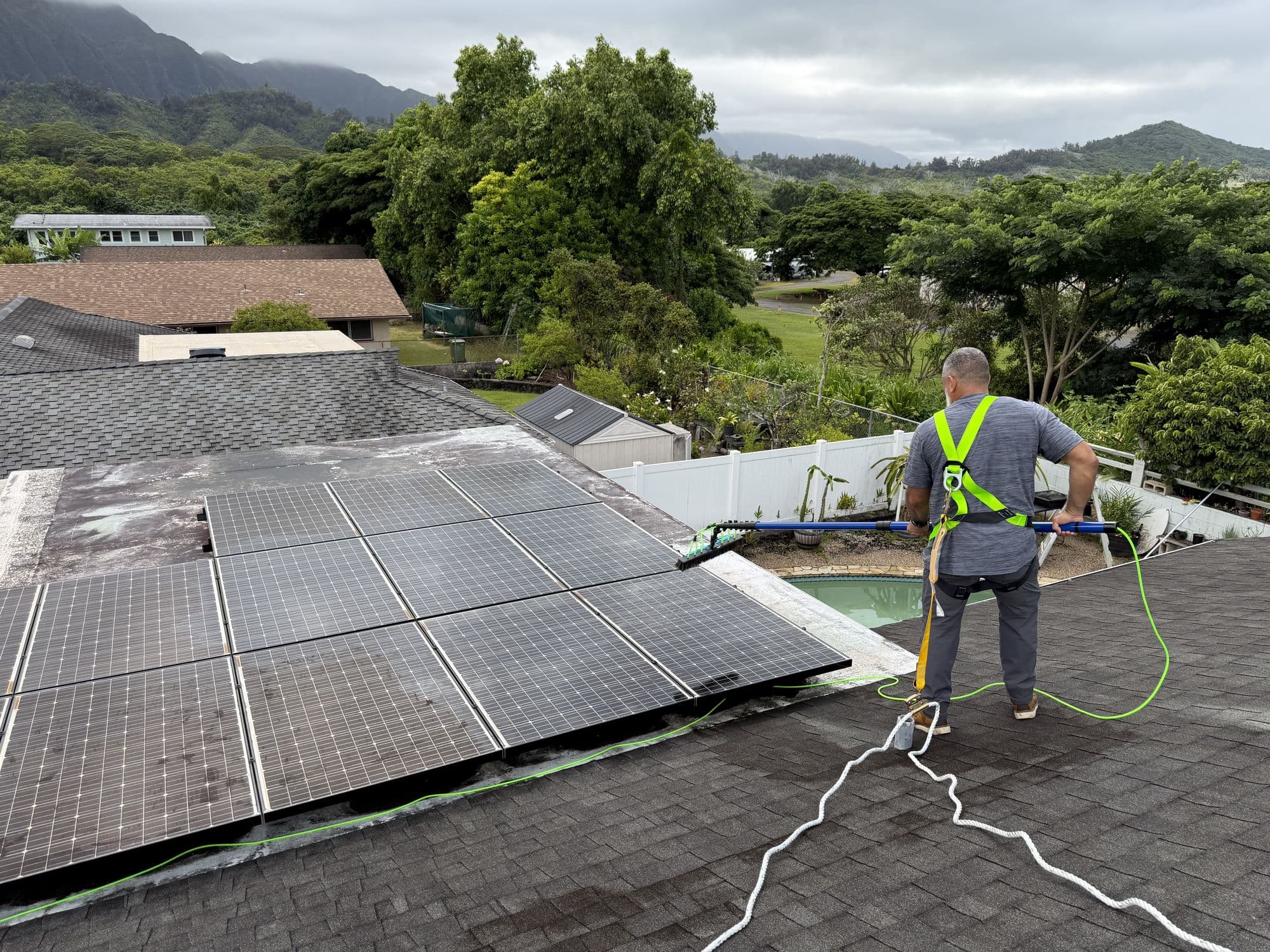 Ari cleaning rooftop solar panels in Kaneohe, the Ko'olau behind
