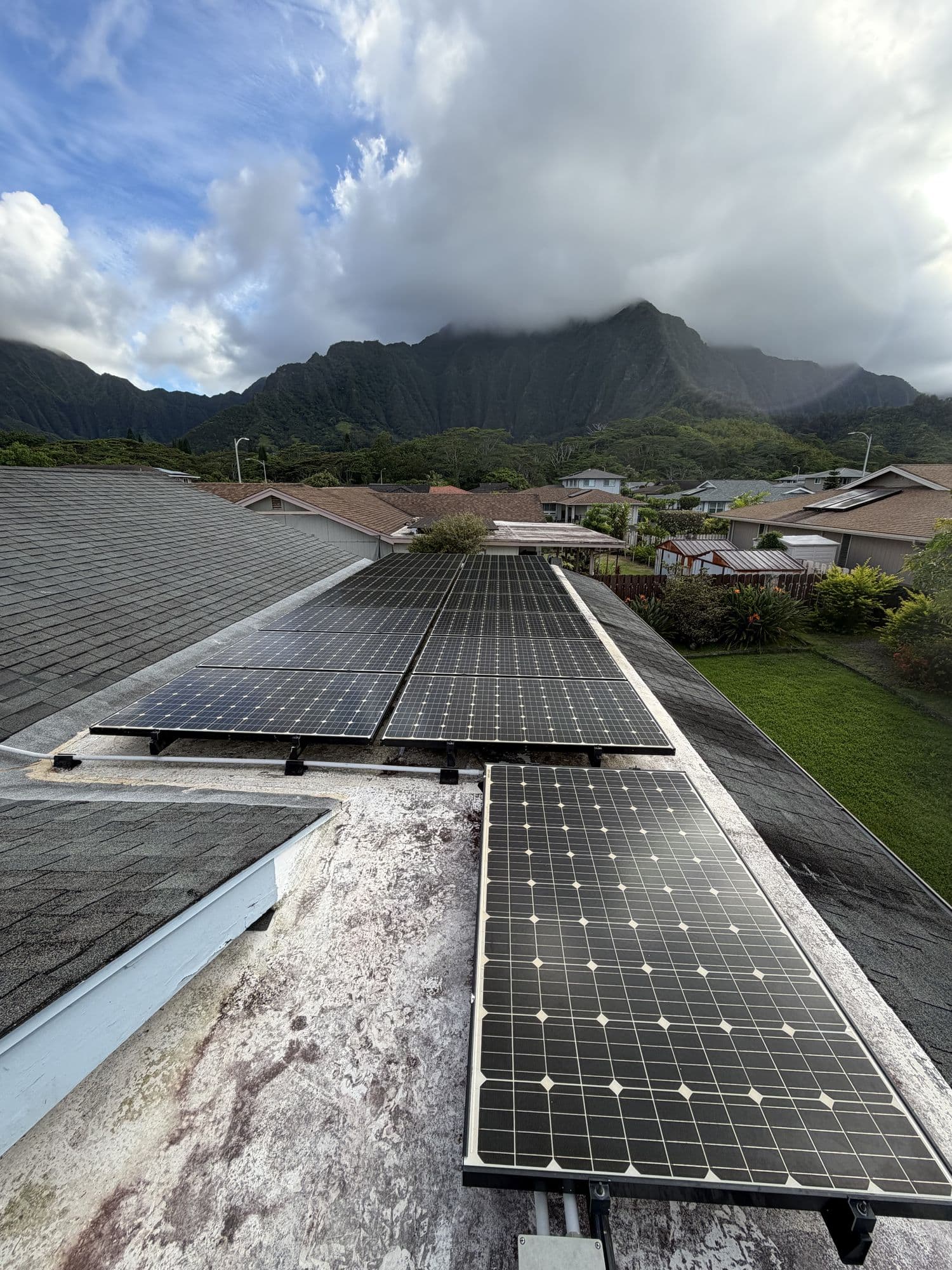 A solar array on a roof with the Ko'olau behind